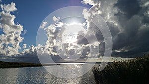 Bright sun above dark clouds over a lake