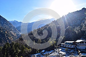 Bright Sun above High Mountains with Golden Sunrays, Trees, and Blue Sky - Landscape in Winter in Himalayan Valley Village, India