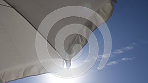 Bright sun in blue sky framed by frill of white beach umbrella flutter on breeze
