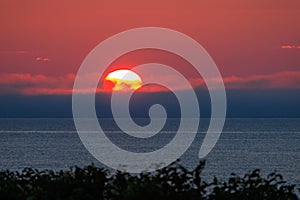 Bright sun and low cloud on ocean horizon with orange sunrise glow in sky