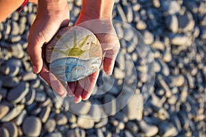 Bright sun painted on pebble in the hands of a child on the background of a pebble beach. Pebbles and sea background