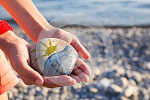 Bright sun painted on pebble in the hands of a child on the background of a pebble beach. Pebbles and sea background