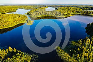 Bright sun shines above blue lakes and green forest, aerial landscape