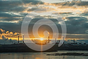 The bright sun shines into the frame against the background of pipes and smoke from the enterprise