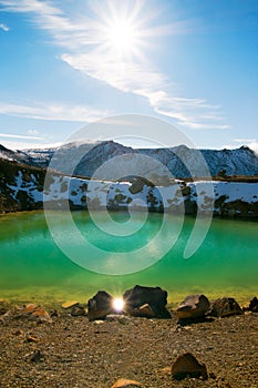 Bright sun is shining and reflecting on the water of unique blue turquoise lake known like Emerald lake in Tongariro National Park