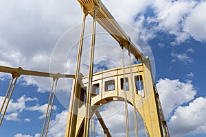 Bright sunlight on the upright structure of a yellow self anchored suspension bridge, deep blue sky with clouds