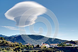Large lenticular cloud hovers over a hillside Spanish village.