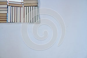 Bright sunny detail of an assortment of books in a white shelf in a room with white textured wall with copy space, back of books