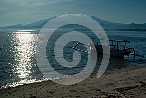 Bright sunny morning on tropical beach, sun glares on water, tradition fishing boat on shore with flag of Indonesia, foggy blue.