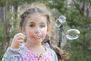 On a bright sunny summer day in the forest, a girl blows soap bubbles