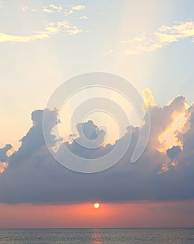 Bright Sunrays Coming through Clouds in Blue Sky with Golden Sun Setting over Ocean