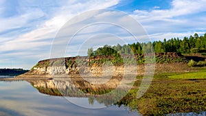 A bright sunset with clouds reflected in the water in Yakutia with clay cliffs of spruce forest in the wild North