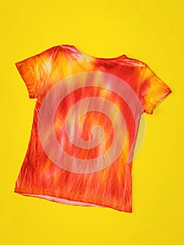 Bright t-shirt in tie dye style on yellow background. Flat lay.