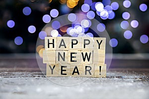 Bright text Happy New Year 2022 on bokeh background written with wooden cubes and snow, colorful festive design