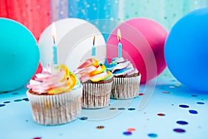 Bright three cupcakes with candles on blue background with colorful air balloons, anniversary celebration