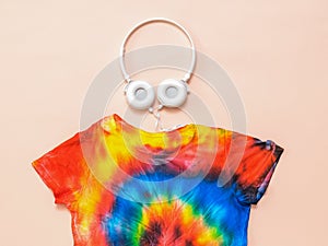 A bright tie dye t-shirt with headphones on a pastel background. Flat lay. Pastel color.