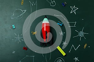 Bright toy rocket, school supplies and drawings on chalkboard, flat lay. Space for text