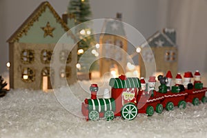 Bright toy train near decorative houses with Christmas lights on artificial snow