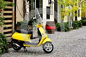 Bright trendy yellow Italian made scooter in old street with cobblestone