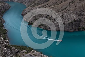 Bright turquoise blue mountain river Sulak with floating red speed boat with curved track on water, depth steep Sulak canyon slope