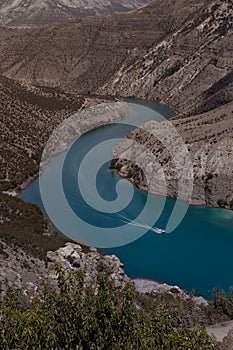 Bright turquoise blue mountain river Sulak with floating red speed boat with curved track on water, depth steep Sulak canyon slope