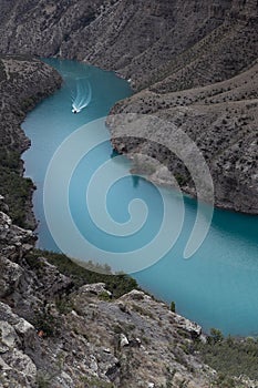 Bright turquoise blue mountain river Sulak with floating red speed boat with white track on water, depth steep Sulak canyon slopes