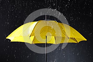 Bright umbrella under rain on dark