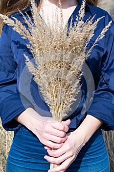 Bright vertical photo of bouquet made of dried autumn bushgrass in young woman hands.