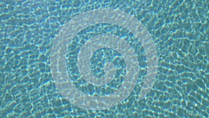 Bright vibrant blue clear water of pool ripples with light reflection. Top view.