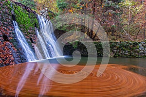 Bright waterfall fduring fall. It is colored by orarge colour from leaves