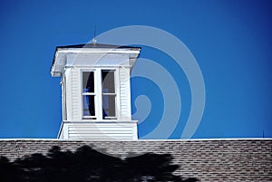Bright white cupola sits on top of barn roof against a deep blue sky