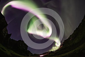 Bright white pink aurora borealis spiral over mountain valley, Iceland