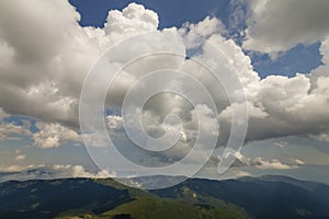 Bright white puffy clouds lit by sun spreading against blue summer sky over green mountain ridge.