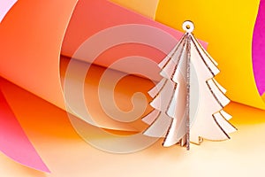 Bright wooden pink Christmas tree on colorful magenta and yellow paper swirls abstract background with copy space. Simple New Year