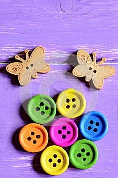 Bright wooden round buttons laid out in the shape of a flower on a green paper sheet, wooden butterfly buttons. Wooden background