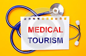 On a bright yellow background, a blue stethoscope and a sheet of paper with the text MEDICAL TOURISM. Medical concept