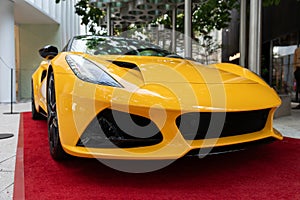 Bright yellow body of modern auto with aerodynamic shape and stylish exterior details. Expensive supercar parked on red