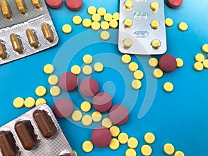 Bright yellow, brown, red and pink tablets of a round and oval shape lie apart on a pink paper background. medical background