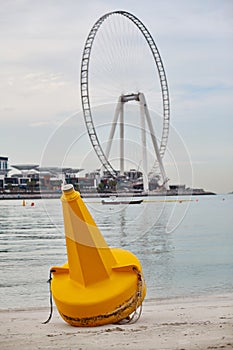 A bright yellow buoy lies on the shore against the background of the island Bluewater and wheels of the Eye Dubai