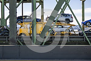 Bright yellow car hauler big rig semi-truck transporting cars on hydraulic semi trailer running on the truss metal bridge
