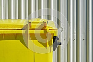 Bright yellow dumpster against a white industrial corrugated cladding or wall siding