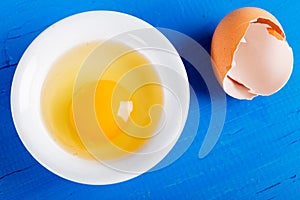Bright yellow egg yolk in white bowl on old wooden table