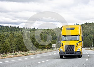 Bright yellow industrial grade professional long haul big rig semi truck transporting cargo in semi trailer climbing on the uphill