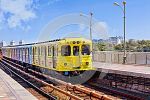 A bright yellow metro train departs from the platform and rushes along the metro bridge in Kyiv to the left side of the city