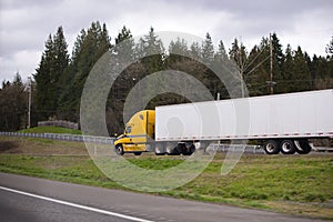 Bright yellow modern semi truck trailer on fencet exit to highway road