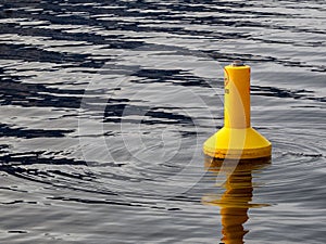 Bright yellow navigation buoy is seen in contrast to wave patterns