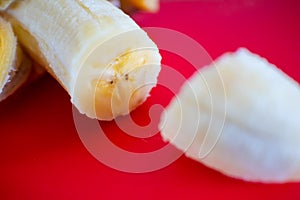 Bright yellow, peeled, bruised and cut banana. Resting on a red cutting board.