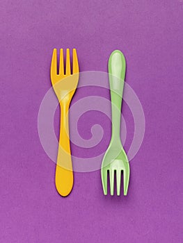Bright yellow plastic spoon and fork on a blue background. Flat lay.Yellow and green plastic forks on a purple background. Minimal