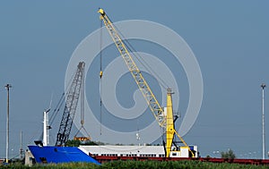 Bright yellow quay crane at work in a harbour dock: Near there is a black crane.