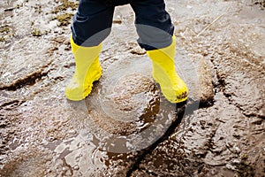 bright yellow rubber boots on the feet of a boy walking through mud, snow and puddles in early spring